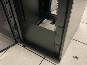 Black server rack with black blanking panels on raised floor system